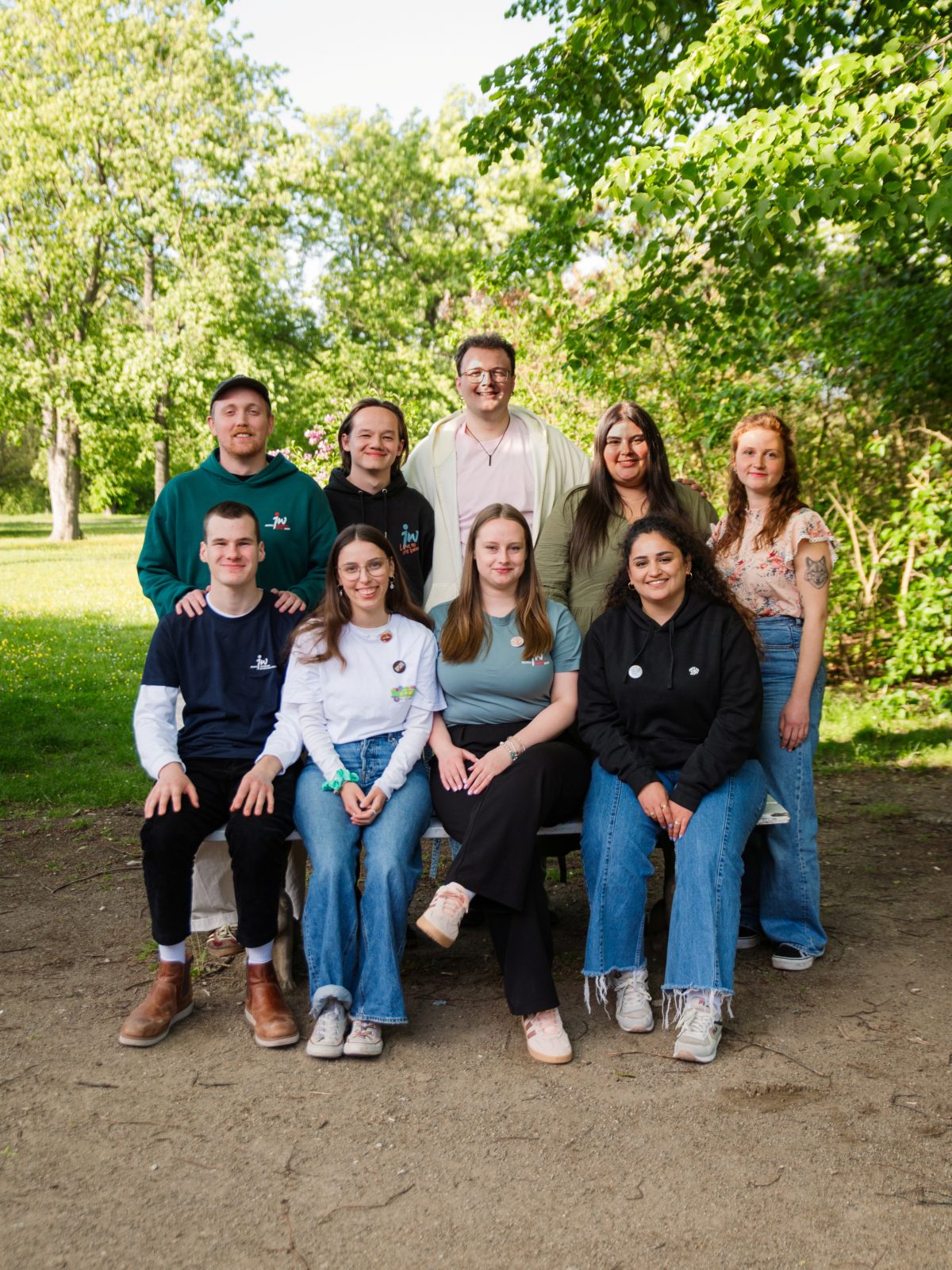 Neun junge Erwachsene posieren lächelnd für ein Gruppenfoto in einem grünen Park